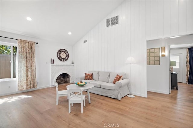 living area with light wood-style floors, a fireplace, vaulted ceiling, visible vents, and baseboards