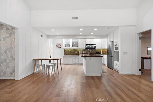 kitchen featuring visible vents, white cabinetry, light wood finished floors, backsplash, and stainless steel refrigerator