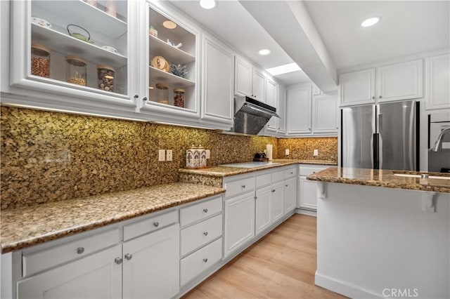 kitchen featuring glass insert cabinets, white cabinets, light stone countertops, decorative backsplash, and stainless steel refrigerator