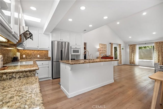 kitchen with white cabinets, oven, stainless steel fridge, a sink, and open floor plan
