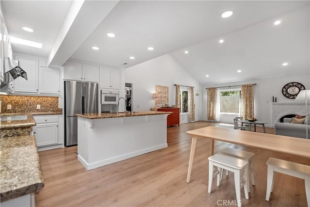 kitchen with light stone countertops, light wood-style flooring, white cabinetry, stainless steel fridge, and open floor plan