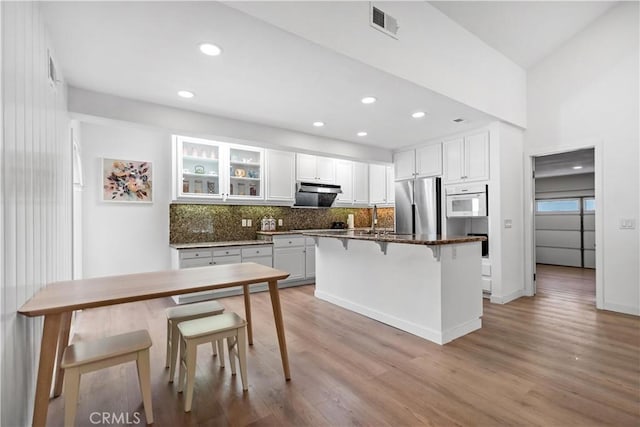 kitchen with freestanding refrigerator, tasteful backsplash, white cabinets, a breakfast bar, and wood finished floors