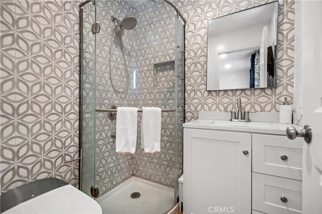 bathroom with vanity, toilet, a stall shower, and wallpapered walls