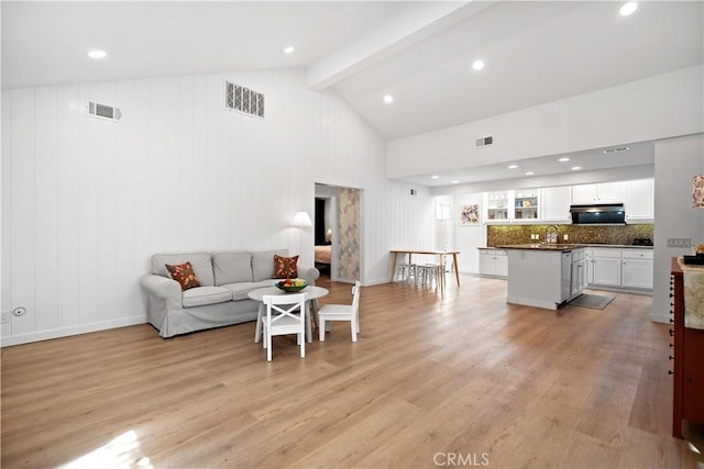 living room featuring visible vents, light wood-style flooring, and vaulted ceiling with beams