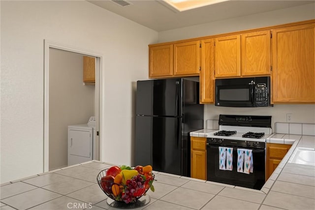 kitchen featuring tile counters, black appliances, washer and dryer, and visible vents
