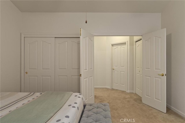 bedroom with a closet, light colored carpet, and baseboards
