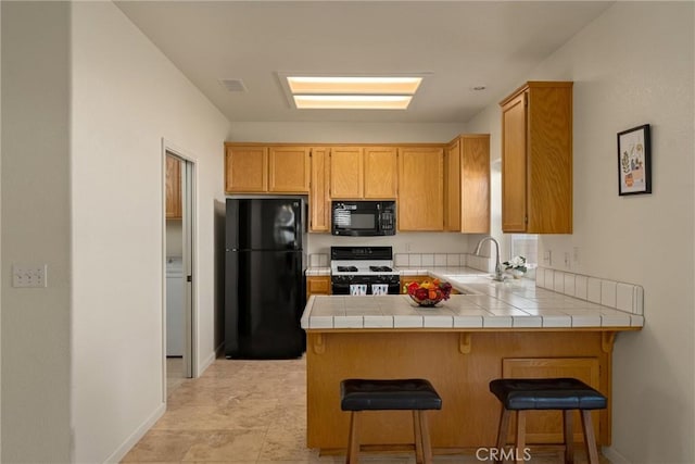 kitchen featuring tile counters, a peninsula, black appliances, a sink, and baseboards