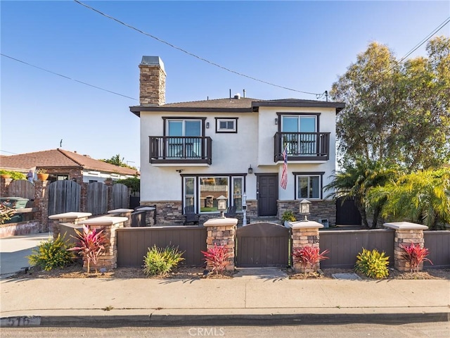 view of front of home featuring a balcony, stucco siding, a chimney, a fenced front yard, and a gate