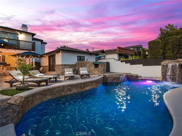 pool at dusk with a patio area, a pool with connected hot tub, and fence