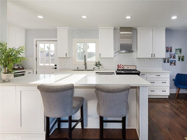 kitchen featuring wall chimney exhaust hood, a sink, light countertops, a breakfast bar, and stainless steel gas stove