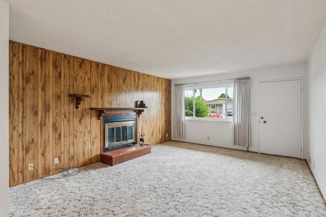 unfurnished living room with a glass covered fireplace, carpet flooring, and wood walls