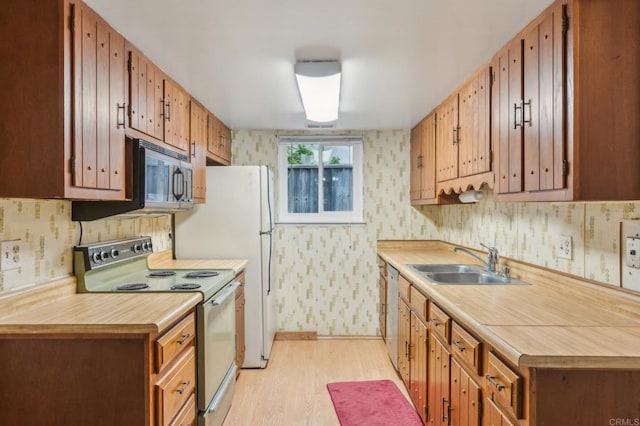 kitchen featuring light wood finished floors, wallpapered walls, white appliances, and a sink