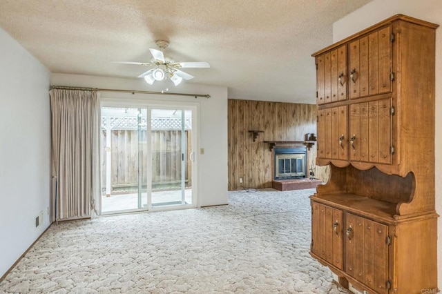living room featuring a textured ceiling, a glass covered fireplace, ceiling fan, light colored carpet, and wood walls