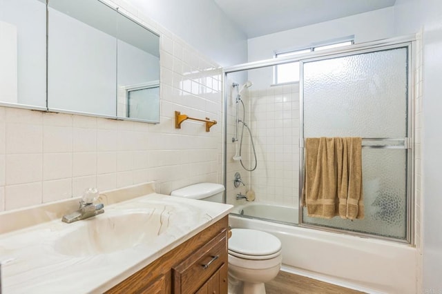 full bath with wood finished floors, vanity, tile walls, enclosed tub / shower combo, and toilet