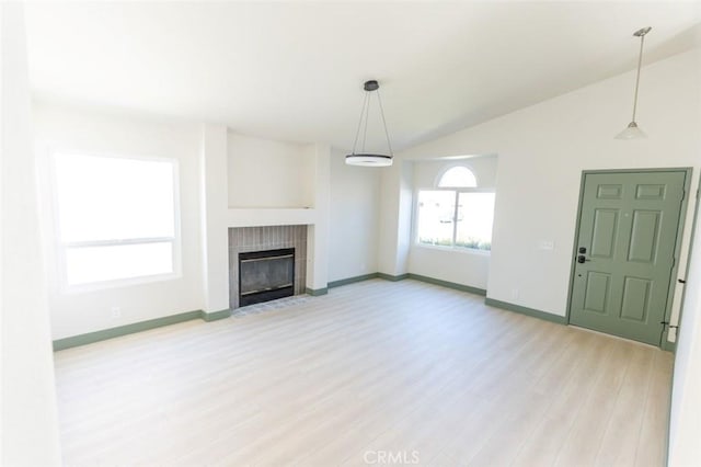 unfurnished living room featuring baseboards, light wood finished floors, a tile fireplace, and lofted ceiling