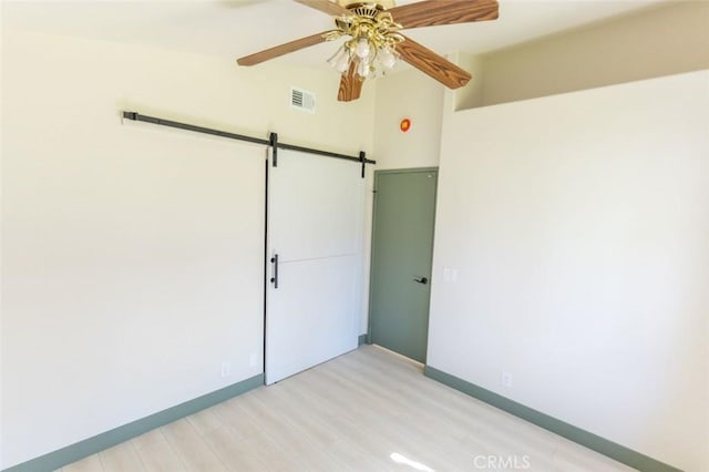 empty room featuring visible vents, baseboards, a barn door, ceiling fan, and light wood-style floors