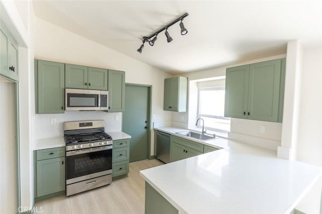 kitchen featuring appliances with stainless steel finishes, a peninsula, lofted ceiling, green cabinetry, and a sink