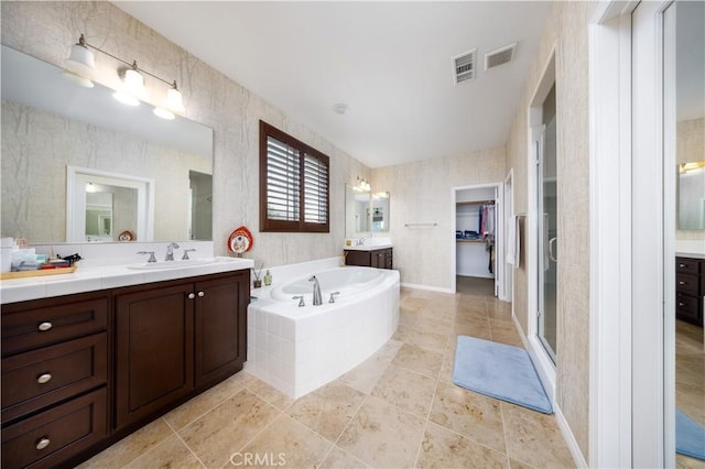 full bath with two vanities, a bath, visible vents, a sink, and a stall shower