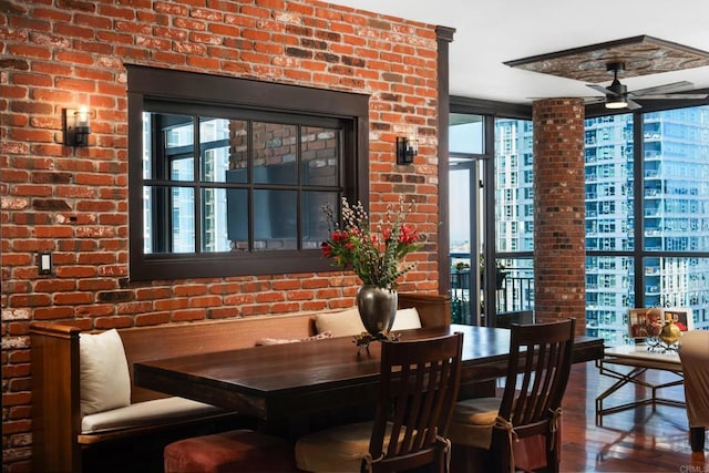 dining area featuring wood finished floors, ceiling fan, and brick wall
