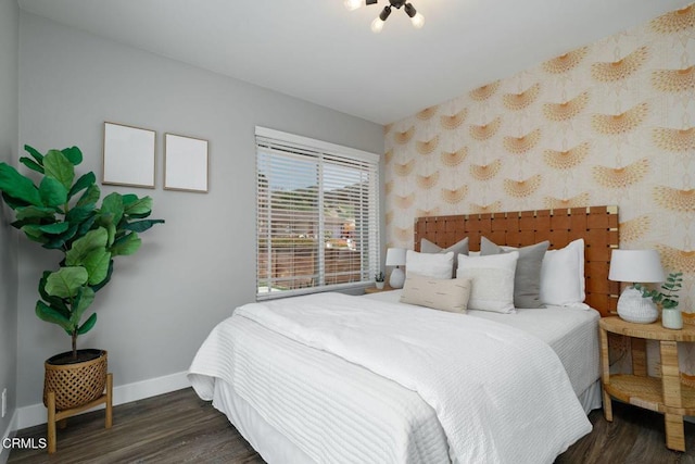 bedroom featuring an accent wall, baseboards, wallpapered walls, and wood finished floors