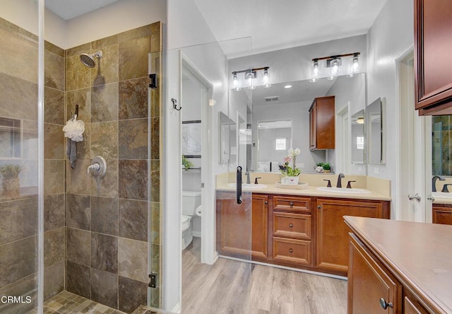 full bathroom featuring a sink, double vanity, toilet, tiled shower, and wood finished floors
