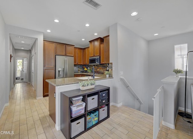kitchen featuring brown cabinets, stainless steel appliances, visible vents, decorative backsplash, and light wood-style flooring