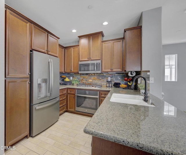 kitchen featuring a sink, recessed lighting, backsplash, light stone counters, and appliances with stainless steel finishes