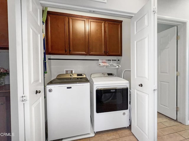 clothes washing area featuring light tile patterned flooring, washer and clothes dryer, and cabinet space