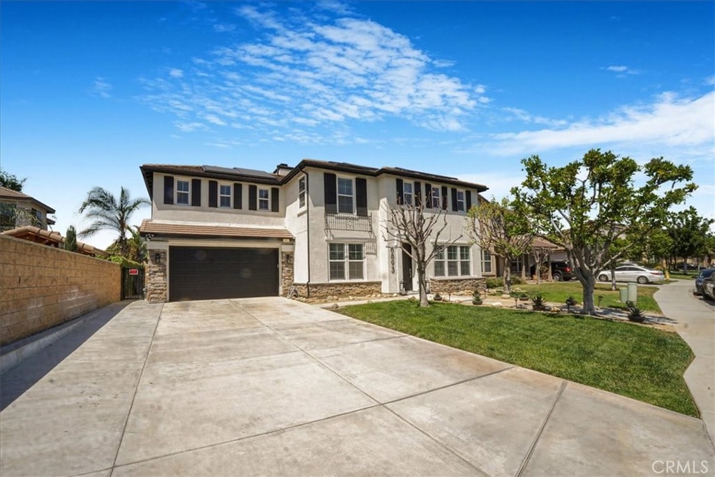 6893 Lancelot Dr, Eastvale, CA 92880 - view of front facade featuring fence, an attached garage, stone siding, concrete driveway, and stucco siding