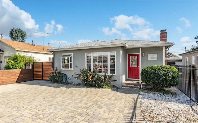 bungalow-style house with a chimney, fence, and stucco siding