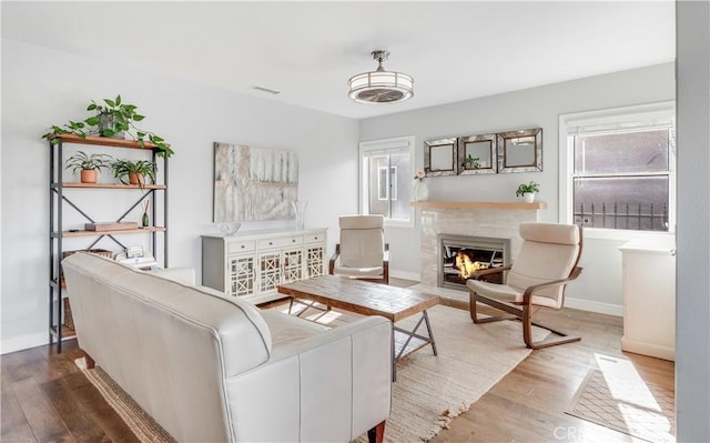living room with a glass covered fireplace, visible vents, baseboards, and wood finished floors