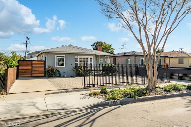 view of front of house featuring a fenced front yard, a chimney, stucco siding, a gate, and driveway