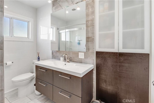 bathroom featuring vanity, tile patterned flooring, a shower with door, toilet, and tile walls