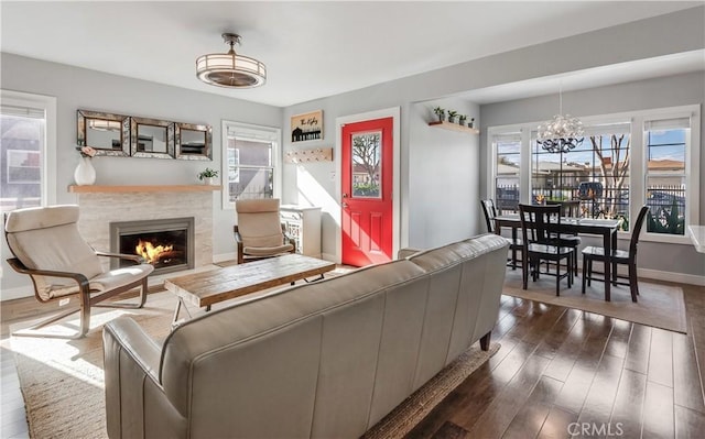 living room featuring a tiled fireplace, baseboards, an inviting chandelier, and dark wood-type flooring