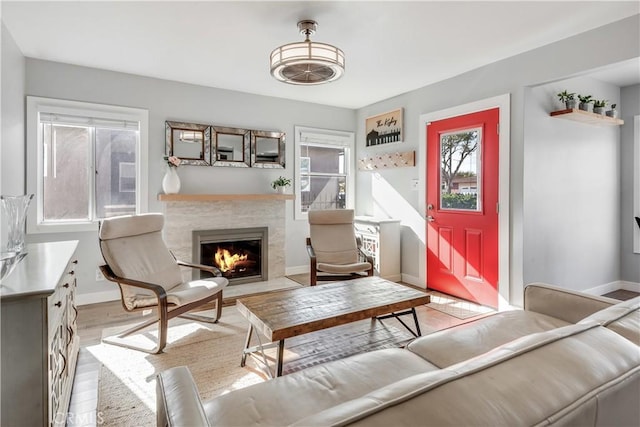 living room featuring a tiled fireplace, light wood finished floors, and baseboards