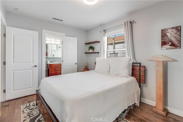 bedroom with visible vents, baseboards, a sink, connected bathroom, and wood finished floors