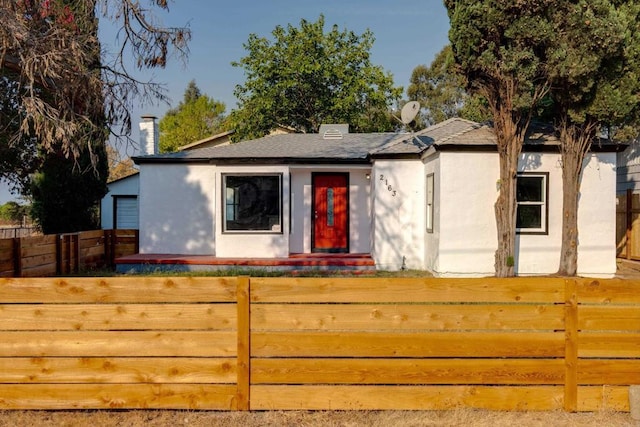view of front of property featuring a chimney, fence, and stucco siding