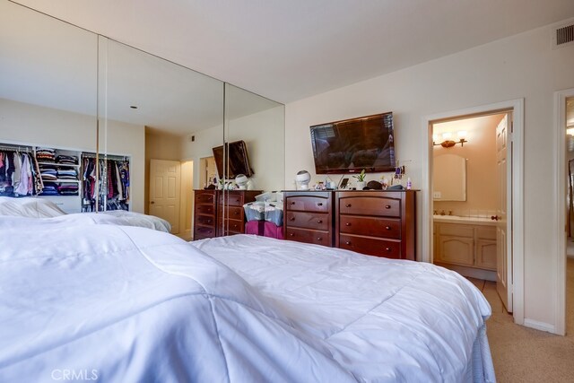 bedroom with visible vents, light colored carpet, and ensuite bathroom