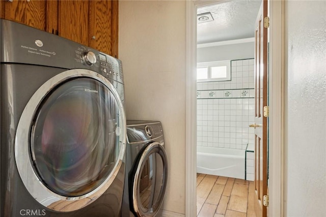 24540 Horst Dr, Crestline, CA 92325 - laundry room featuring crown molding, light wood-style flooring, a textured ceiling, washing machine and clothes dryer, and cabinet space
