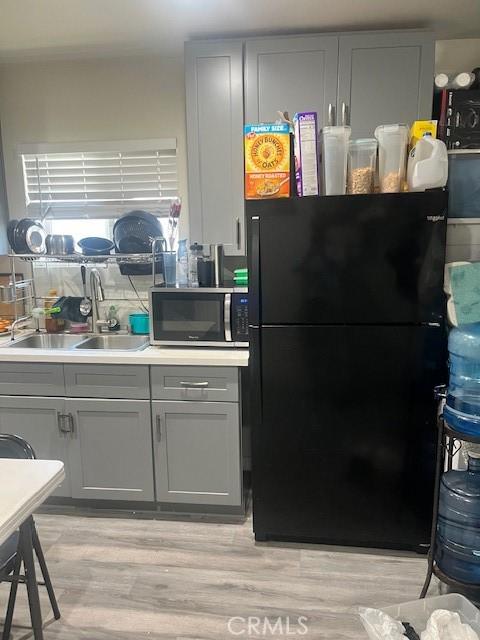 kitchen with stainless steel microwave, gray cabinets, freestanding refrigerator, light wood-style floors, and a sink