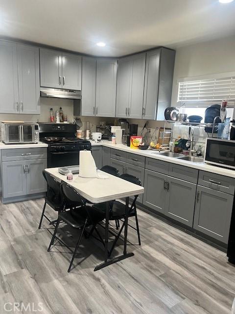 kitchen with light wood finished floors, gray cabinetry, under cabinet range hood, and black gas range oven
