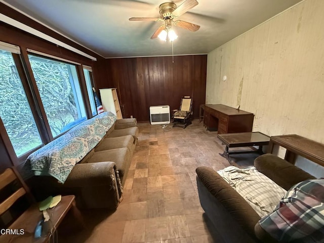 living area featuring wooden walls, heating unit, plenty of natural light, and a ceiling fan