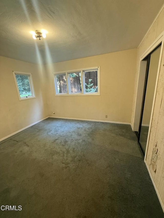 unfurnished bedroom with dark carpet, a closet, baseboards, and multiple windows