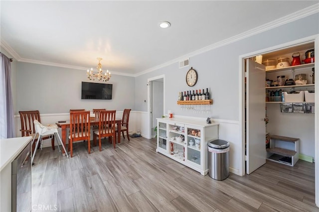 dining space with a notable chandelier, ornamental molding, a wainscoted wall, visible vents, and light wood finished floors