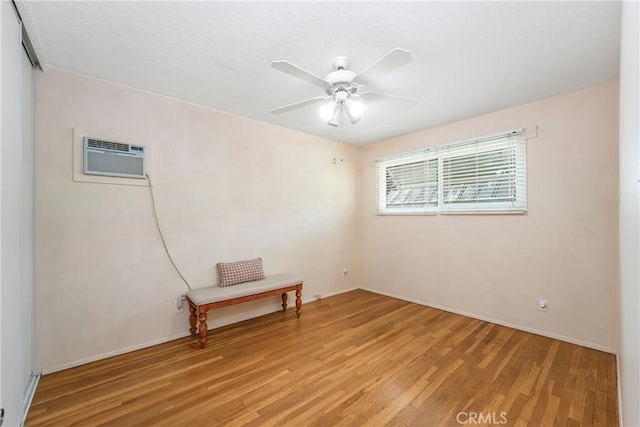empty room with ceiling fan, light wood-type flooring, baseboards, and a wall mounted air conditioner