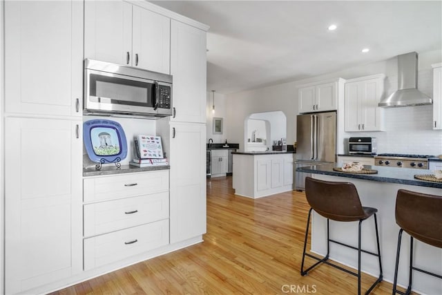 4368 Adams Ave, San Diego, CA 92116 - kitchen featuring wall chimney exhaust hood, stainless steel appliances, a kitchen bar, light wood-style flooring, and white cabinets
