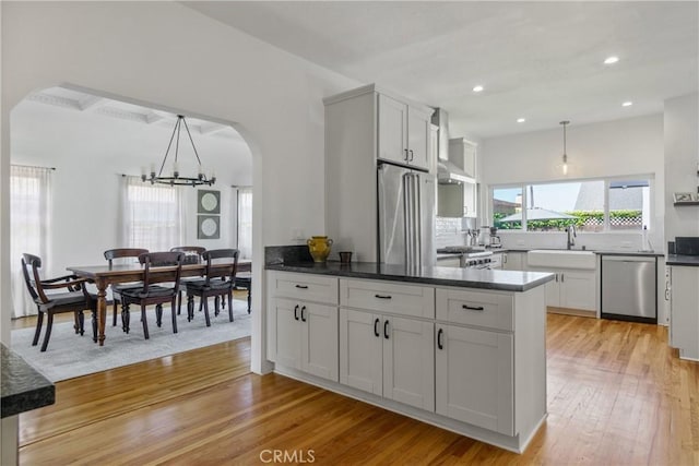 4368 Adams Ave, San Diego, CA 92116 - kitchen with stainless steel appliances, arched walkways, wall chimney range hood, a chandelier, and light wood-style floors