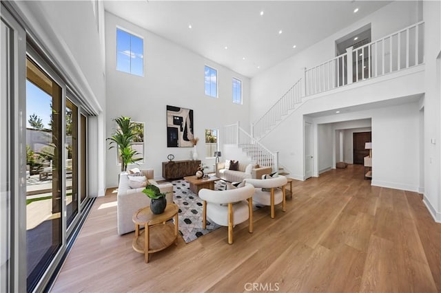 living area with a high ceiling, light wood finished floors, stairs, and a healthy amount of sunlight