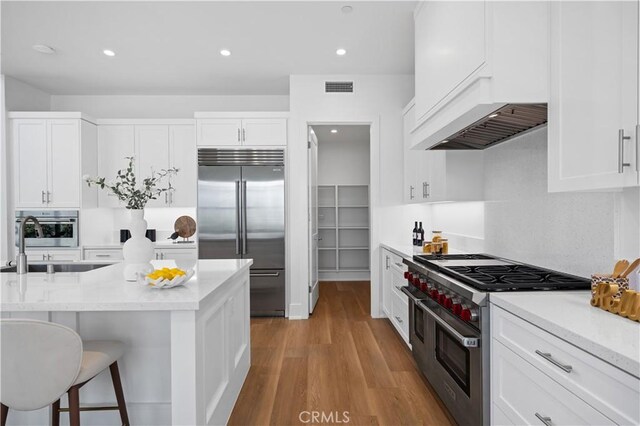 kitchen with a sink, visible vents, premium appliances, white cabinetry, and under cabinet range hood
