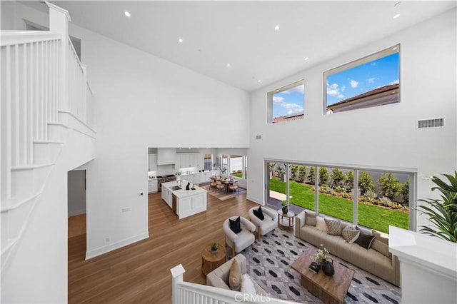 living area featuring recessed lighting, a high ceiling, wood finished floors, visible vents, and baseboards